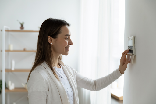 A woman adjusting a thermostat during the summer.
