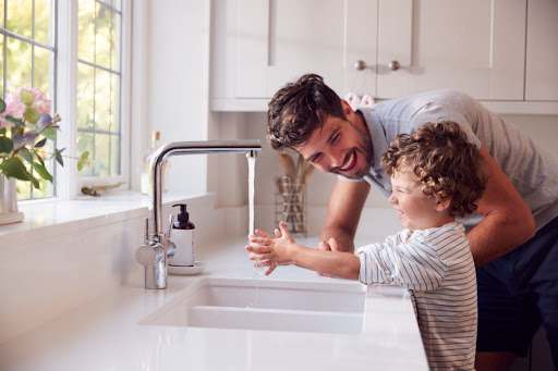 A father and son using a kitchen sink to wash their hands.