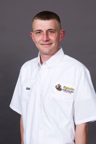 A man wearing a white button-up shirt with a name tag reading "Alex" and embroidered Squeaks logo on the chest stands against a plain, gray background.
