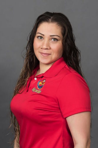 A woman with long dark hair wearing a red polo shirt with an embroidered Squeaks logo stands in front of a plain gray background.