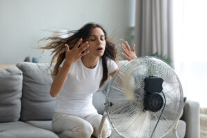 Woman with a broken AC sitting in front of fan to cool down