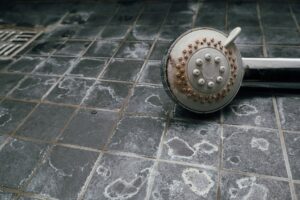 Shower head on shower floor, all of which is covered in limescale.