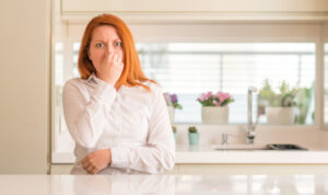 Woman in the kitchen holding nose because of stinky drain.