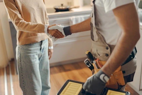 Close up of plumber in uniform shaking hands with female home owner in kitchen